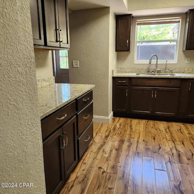 kitchen with light hardwood / wood-style floors, dark brown cabinets, sink, and light stone countertops