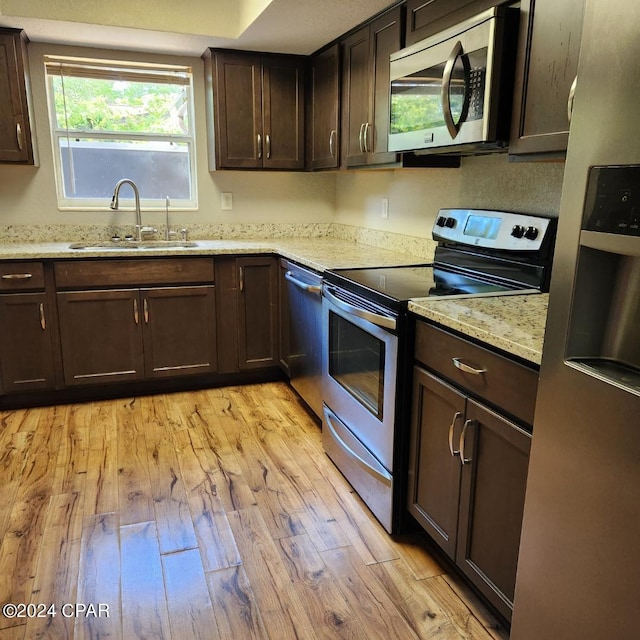 kitchen featuring light wood-type flooring, stainless steel appliances, sink, light stone counters, and dark brown cabinetry