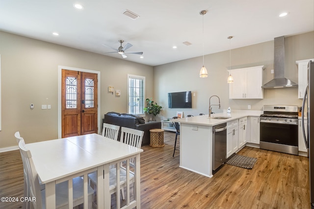 kitchen with kitchen peninsula, appliances with stainless steel finishes, wall chimney range hood, and light wood-type flooring