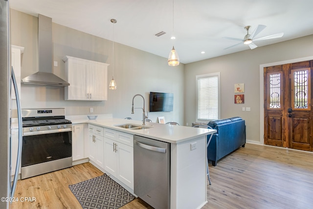 kitchen with appliances with stainless steel finishes, light hardwood / wood-style flooring, wall chimney range hood, and kitchen peninsula