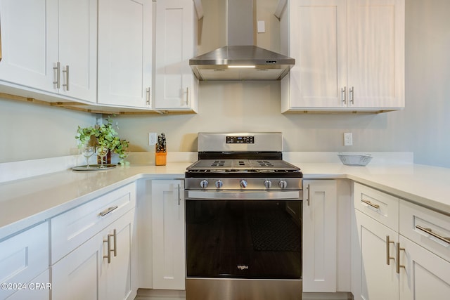 kitchen with wall chimney exhaust hood, stainless steel range with gas cooktop, and white cabinetry