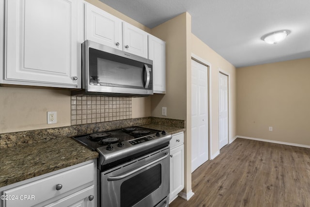 kitchen featuring white cabinetry, stainless steel appliances, tasteful backsplash, dark stone countertops, and wood-type flooring