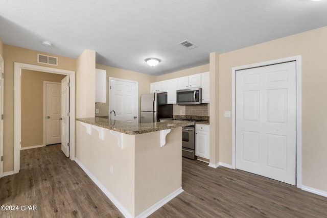 kitchen with dark wood-type flooring, white cabinets, appliances with stainless steel finishes, kitchen peninsula, and a breakfast bar area