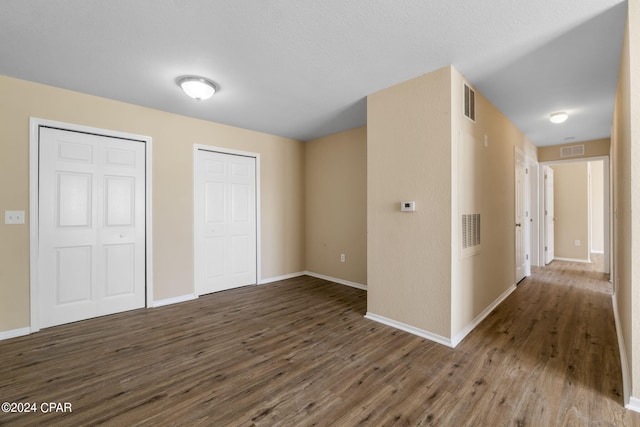 unfurnished bedroom with a textured ceiling, dark wood-type flooring, and two closets