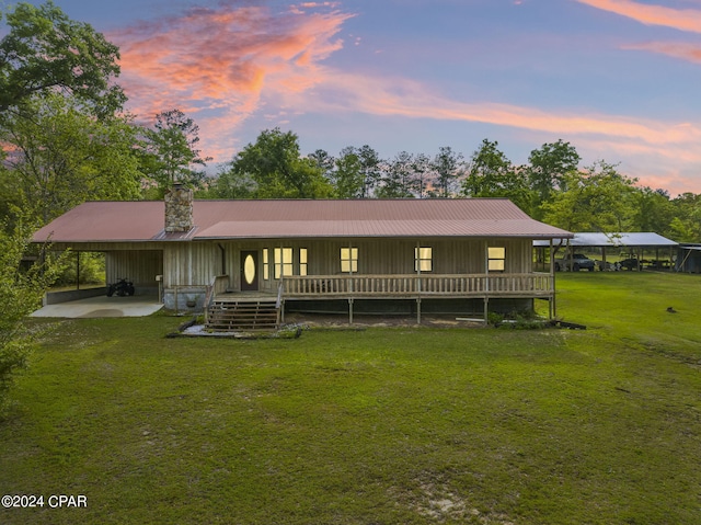 back house at dusk featuring a carport and a lawn