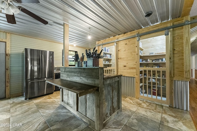 kitchen with a barn door, ceiling fan, stainless steel fridge, and tile floors