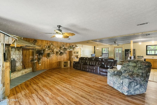 living room with a textured ceiling, ceiling fan, light hardwood / wood-style floors, and wooden walls