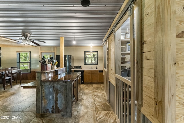 interior space featuring ceiling fan, a barn door, a kitchen island, light tile flooring, and dark stone countertops