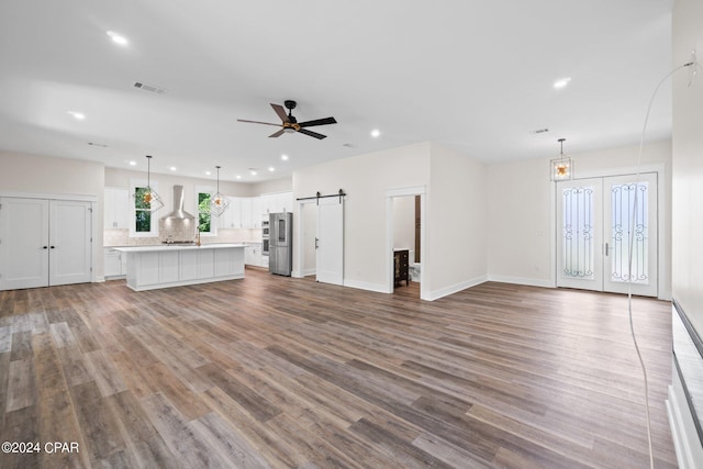 unfurnished living room featuring a barn door, wood-type flooring, and ceiling fan