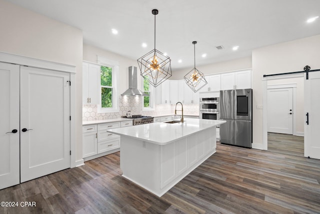 kitchen featuring appliances with stainless steel finishes, a barn door, dark wood-type flooring, and wall chimney exhaust hood