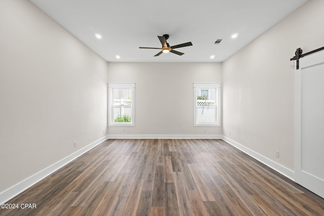 spare room featuring dark wood-type flooring, a barn door, and ceiling fan