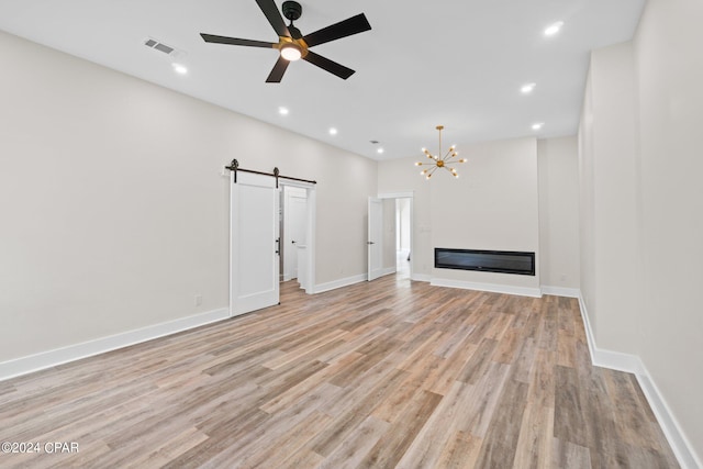 unfurnished living room with ceiling fan with notable chandelier, a barn door, and light wood-type flooring