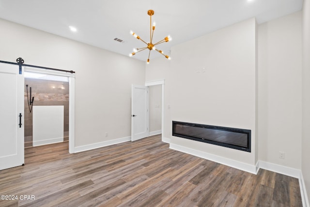 unfurnished living room with wood-type flooring, a notable chandelier, and a barn door