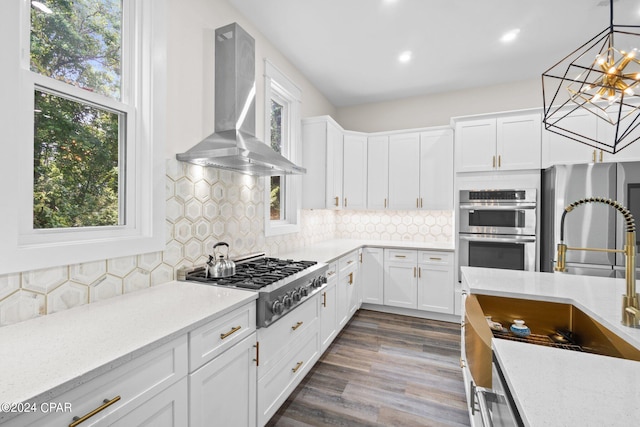 kitchen featuring tasteful backsplash, wall chimney range hood, dark wood-type flooring, stainless steel appliances, and pendant lighting