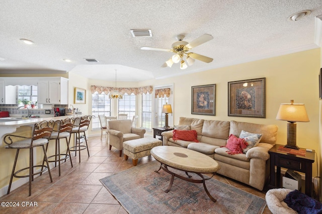 living room featuring a textured ceiling, sink, light tile flooring, ceiling fan with notable chandelier, and crown molding