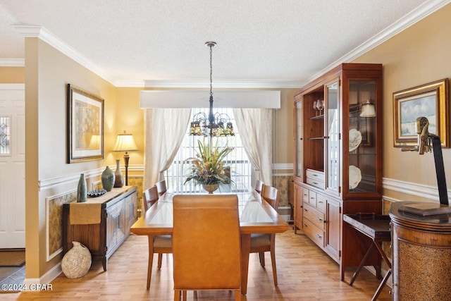 dining space featuring a textured ceiling, light wood-type flooring, a chandelier, and ornamental molding