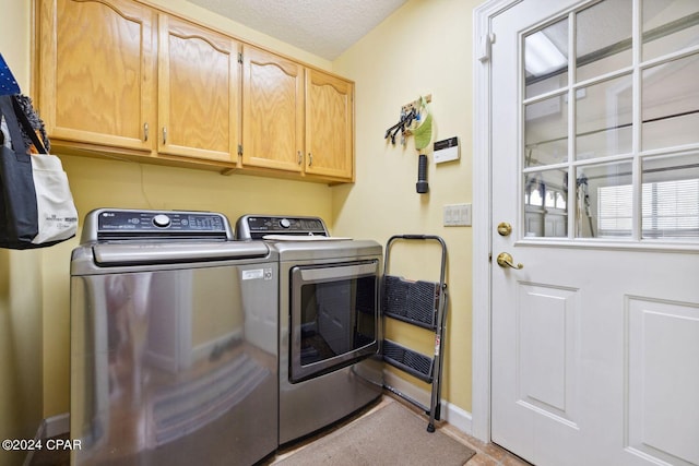 washroom featuring washing machine and clothes dryer, cabinets, and a textured ceiling