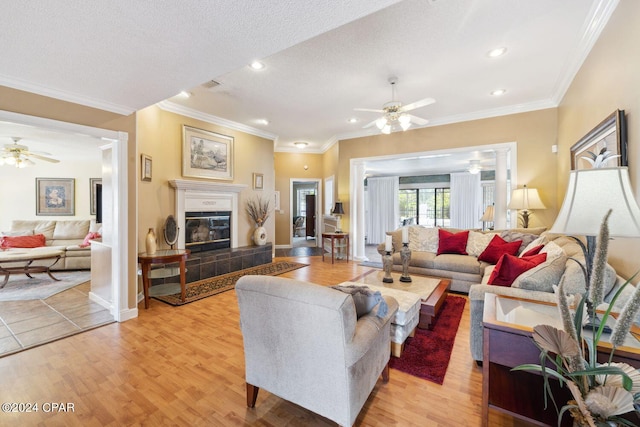 tiled living room featuring a textured ceiling, ceiling fan, ornamental molding, and a tiled fireplace