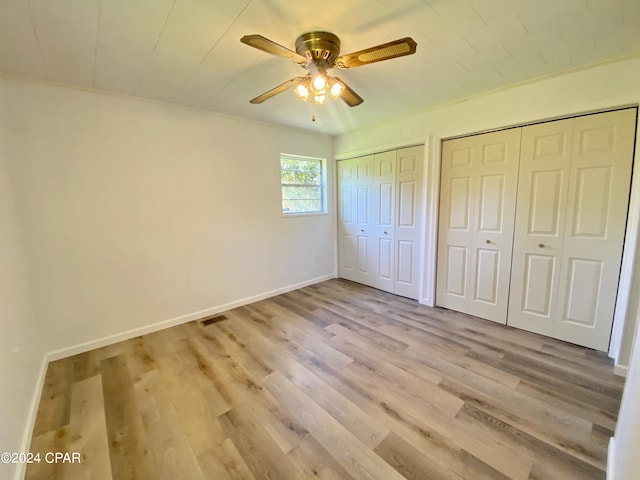 unfurnished bedroom with ceiling fan, light wood-type flooring, and two closets