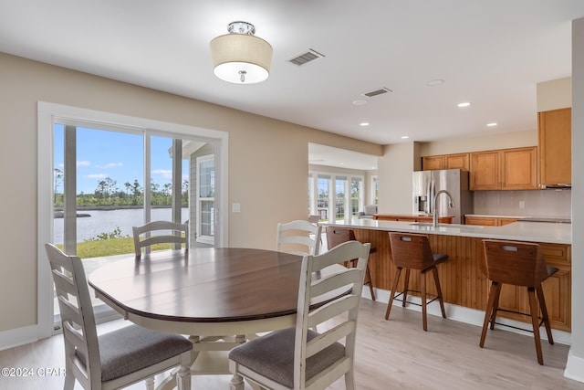 dining space with light wood-type flooring, a water view, and sink