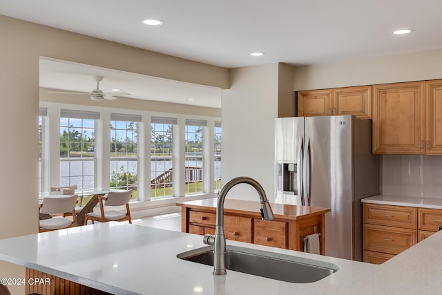 kitchen with a water view, stainless steel fridge, backsplash, sink, and ceiling fan