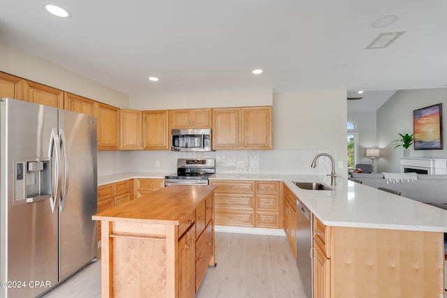 kitchen with stainless steel appliances, light hardwood / wood-style floors, sink, kitchen peninsula, and butcher block counters