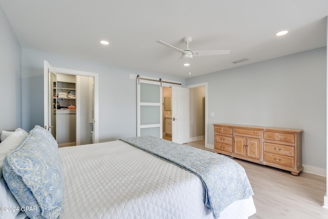 bedroom featuring light wood-type flooring, ceiling fan, a closet, a spacious closet, and a barn door