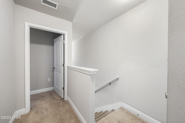 hallway with light carpet and a textured ceiling