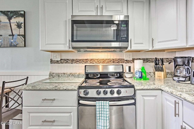 kitchen featuring white cabinets, light stone countertops, tasteful backsplash, and range