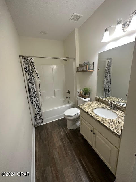 full bathroom with shower / bath combo with shower curtain, a textured ceiling, oversized vanity, hardwood / wood-style floors, and toilet