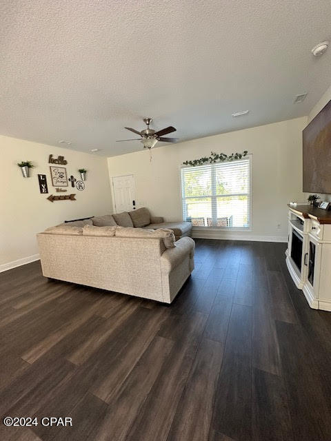 living room with ceiling fan, dark hardwood / wood-style floors, and a textured ceiling