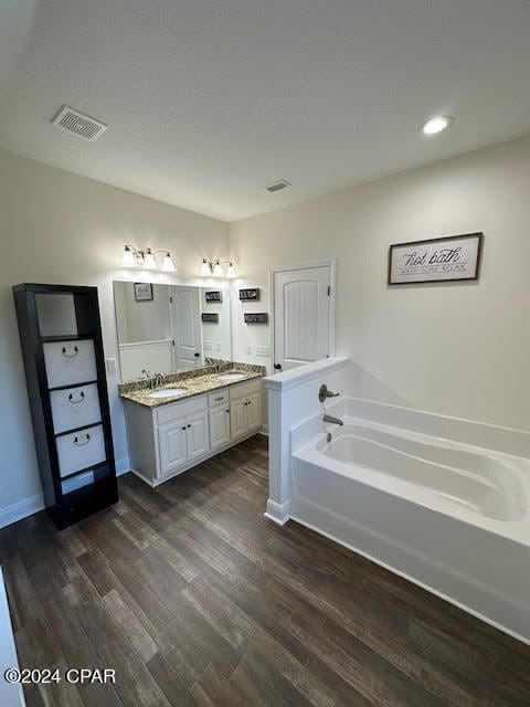 bathroom with dual bowl vanity, a tub, hardwood / wood-style flooring, and a textured ceiling