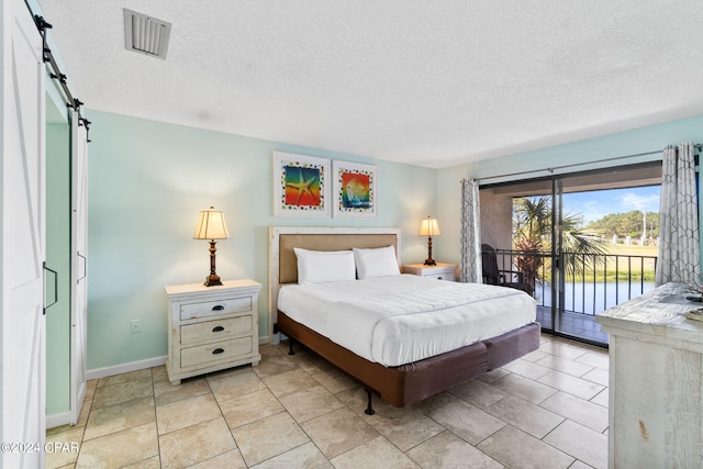 bedroom featuring a textured ceiling, access to outside, light tile floors, and a barn door