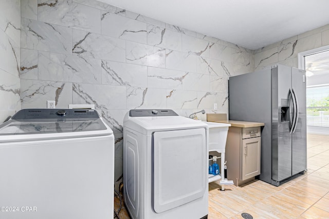 laundry area with tile walls, washing machine and clothes dryer, cabinets, and light tile patterned floors