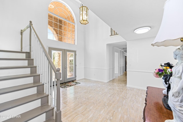 foyer featuring a towering ceiling, tile patterned flooring, french doors, and an inviting chandelier