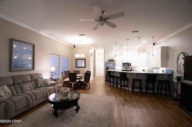 living room with sink, crown molding, hardwood / wood-style flooring, and ceiling fan with notable chandelier