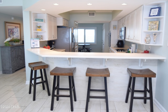 kitchen featuring white cabinets, kitchen peninsula, stainless steel appliances, and a breakfast bar area