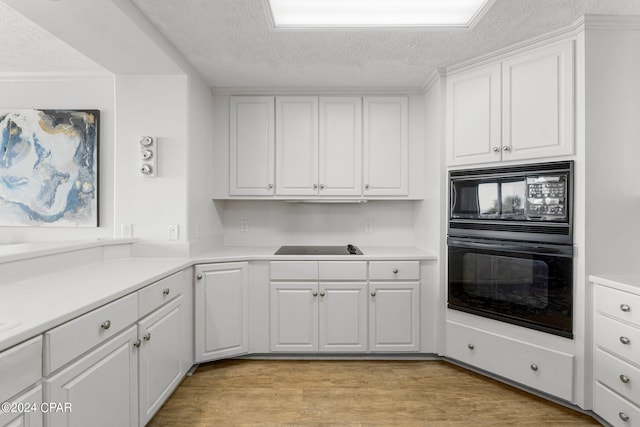 kitchen with white cabinets, black appliances, a textured ceiling, and light wood-type flooring