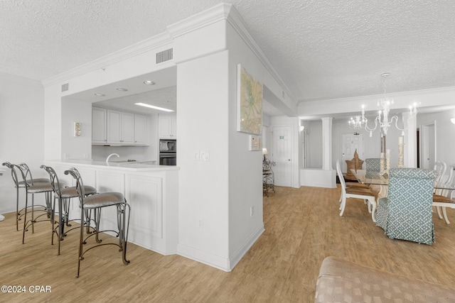 kitchen featuring white cabinets, a notable chandelier, light wood-type flooring, and a kitchen breakfast bar