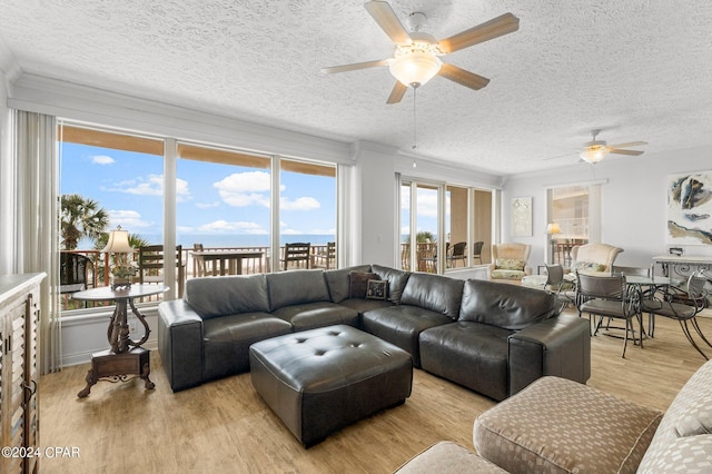 living room featuring a water view, ceiling fan, a textured ceiling, and light wood-type flooring