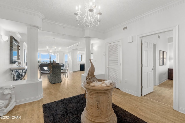 entryway with ornate columns, an inviting chandelier, crown molding, and light wood-type flooring