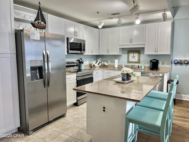 kitchen featuring a center island, a kitchen breakfast bar, stainless steel appliances, light stone countertops, and white cabinets