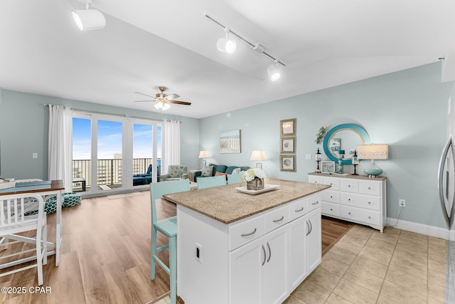 kitchen with a breakfast bar, a kitchen island, ceiling fan, light hardwood / wood-style floors, and white cabinets