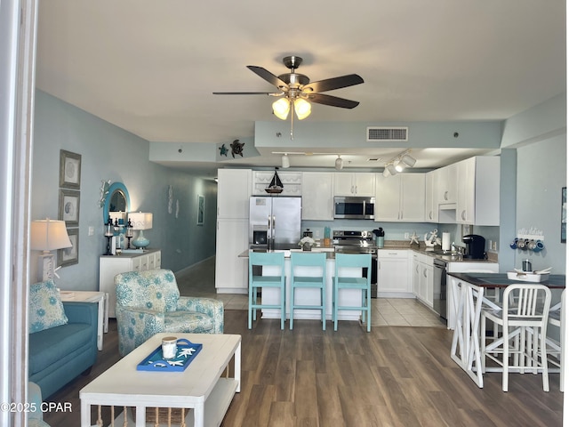 kitchen with dark wood-type flooring, ceiling fan, stainless steel appliances, a kitchen breakfast bar, and white cabinets