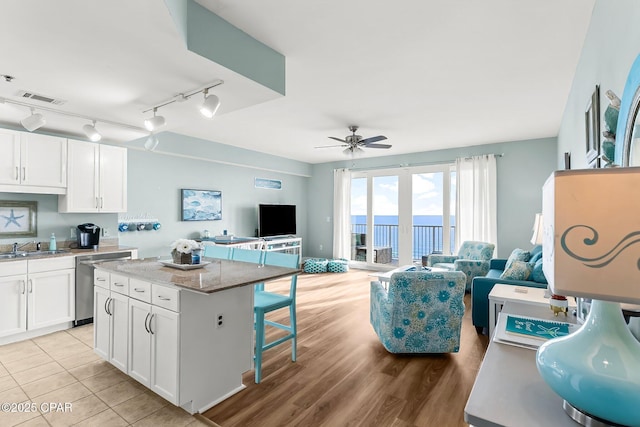 kitchen featuring a center island, stainless steel dishwasher, a kitchen breakfast bar, ceiling fan, and white cabinets