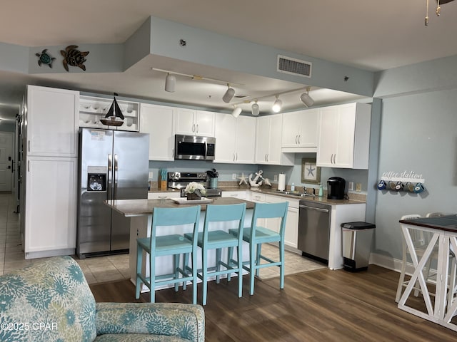 kitchen with white cabinetry, a kitchen breakfast bar, stainless steel appliances, a center island, and wood-type flooring