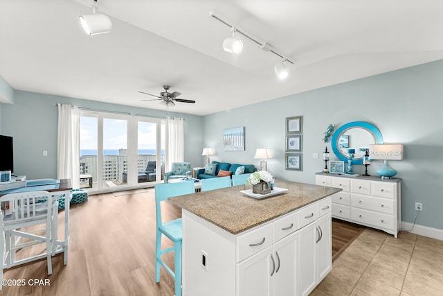 kitchen featuring white cabinetry, a breakfast bar area, a center island, ceiling fan, and light stone countertops