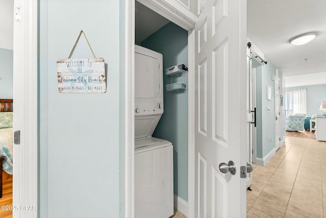 laundry area with light tile patterned floors, a barn door, and stacked washer / dryer