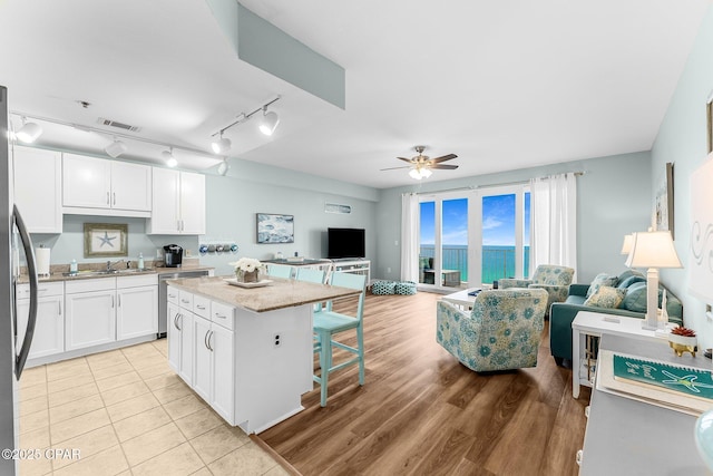 kitchen featuring white cabinetry, a breakfast bar area, a center island, ceiling fan, and light stone counters