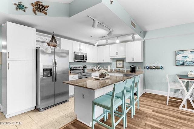 kitchen with appliances with stainless steel finishes, a breakfast bar, dark stone countertops, white cabinets, and a center island